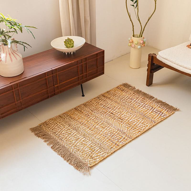 Woven Natural Area Rug with diamond pattern, fringed edges, laid on white floor near wooden cabinet.